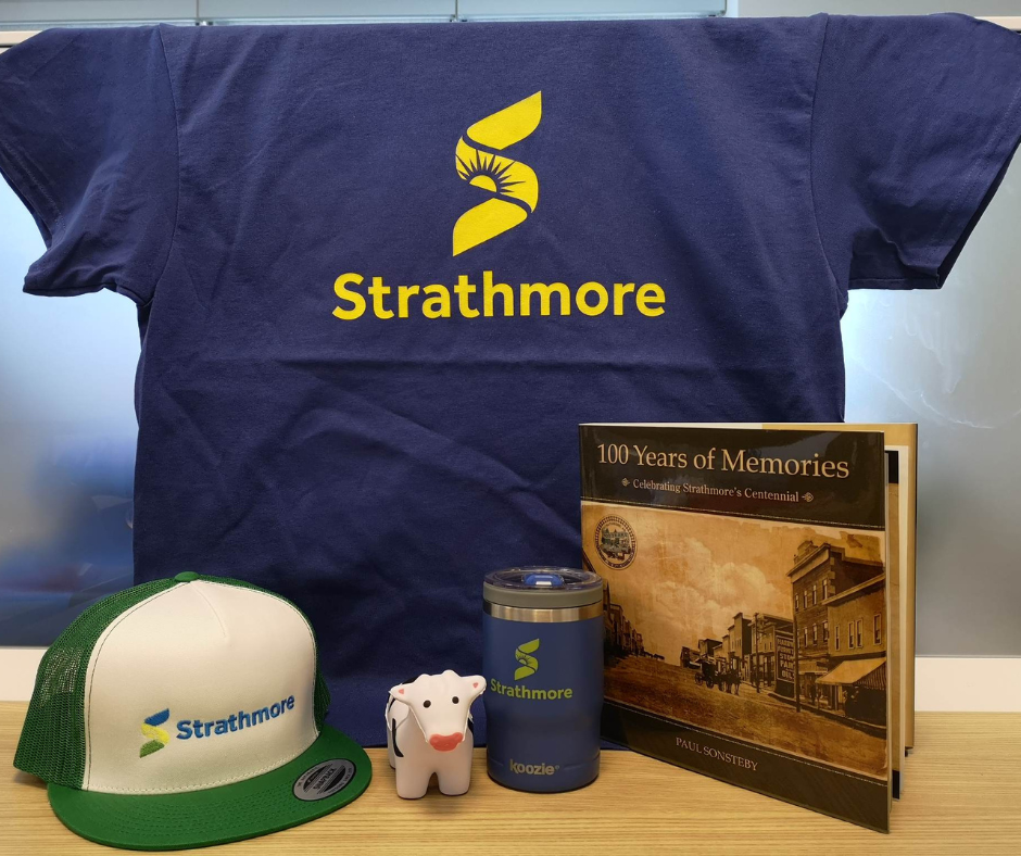 Picture of Strathmore branded blue T-shirt, Green Strathmore Trucker's Hat, Small cow toy, Strathmore Branded tumbler and a copy of Paul Sonteby's book, "100 Year's of Memories"