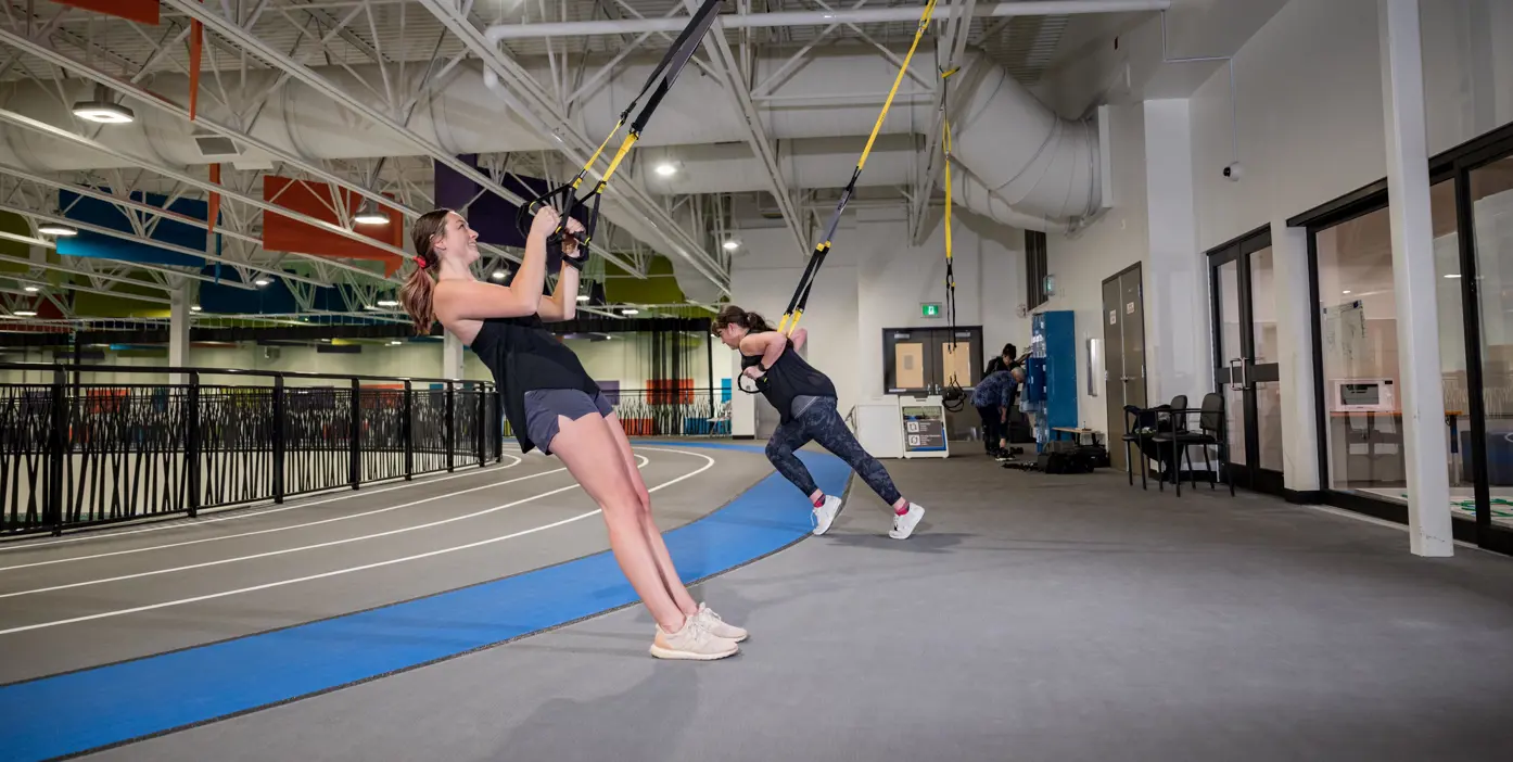 A man hangs forward using TRX equipment on a green background, Text overlay, TRX. 