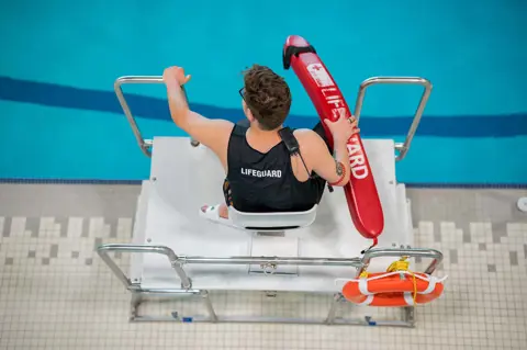 a lifeguard sits in a lifeguard chair overlooking a pool. Text overlay: Certification Courses. 