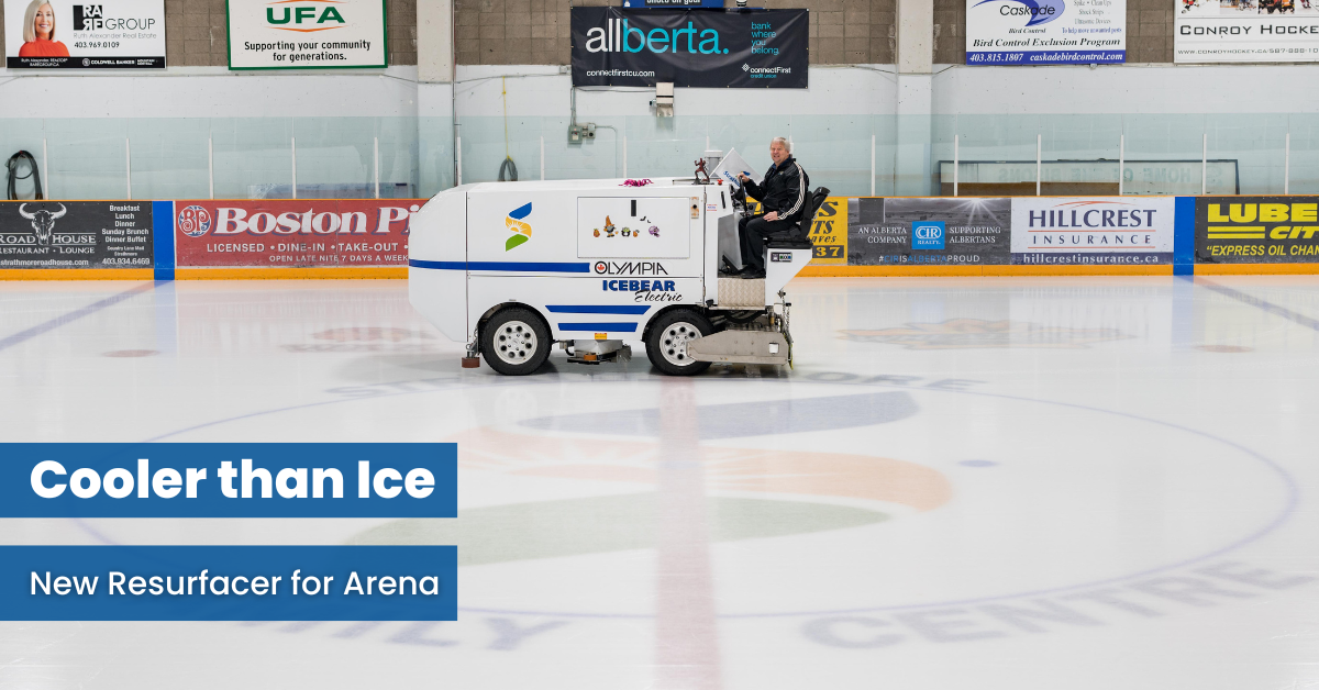 Mayor Fule sits in the driver's seat of a new ice resurfacer. The machine is in the centre of one of the Town's indoor ice rinks. Advertisements for local businesses are on the walls of the rink.