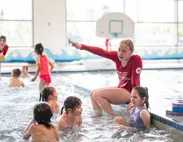 A swim instructor is in an indoor pool teaching several children. Text Overlay: Programs and Lessons